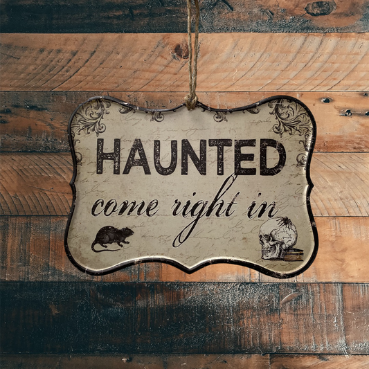 Hanging Sign that says Haunted come right in and has an image of a skull and a rat in the bottom corners. The Sign is hanging from a wooden wall