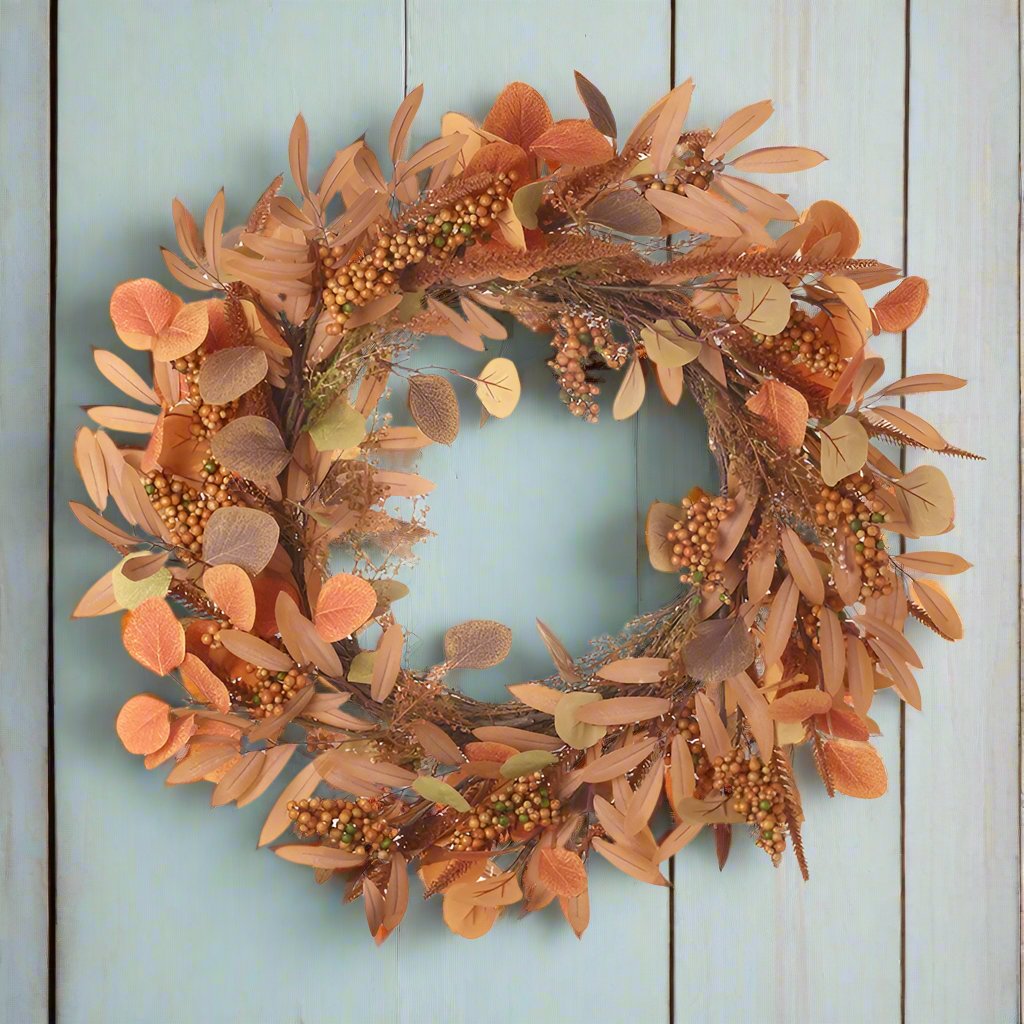 A round wreath made up of various artificial autumn-colored foliage pieces arranged to form a circle.