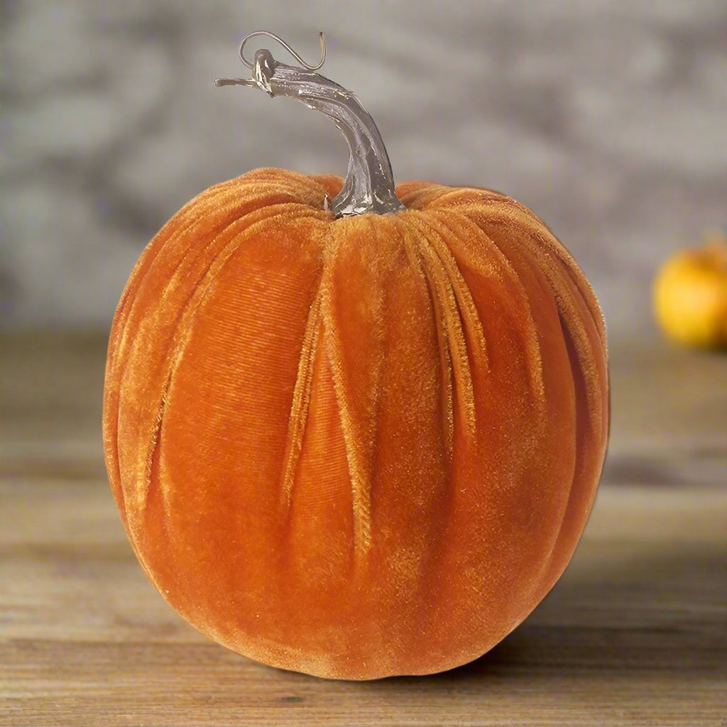 A plush orange velvet pumpkin decoration placed on a wooden surface.
