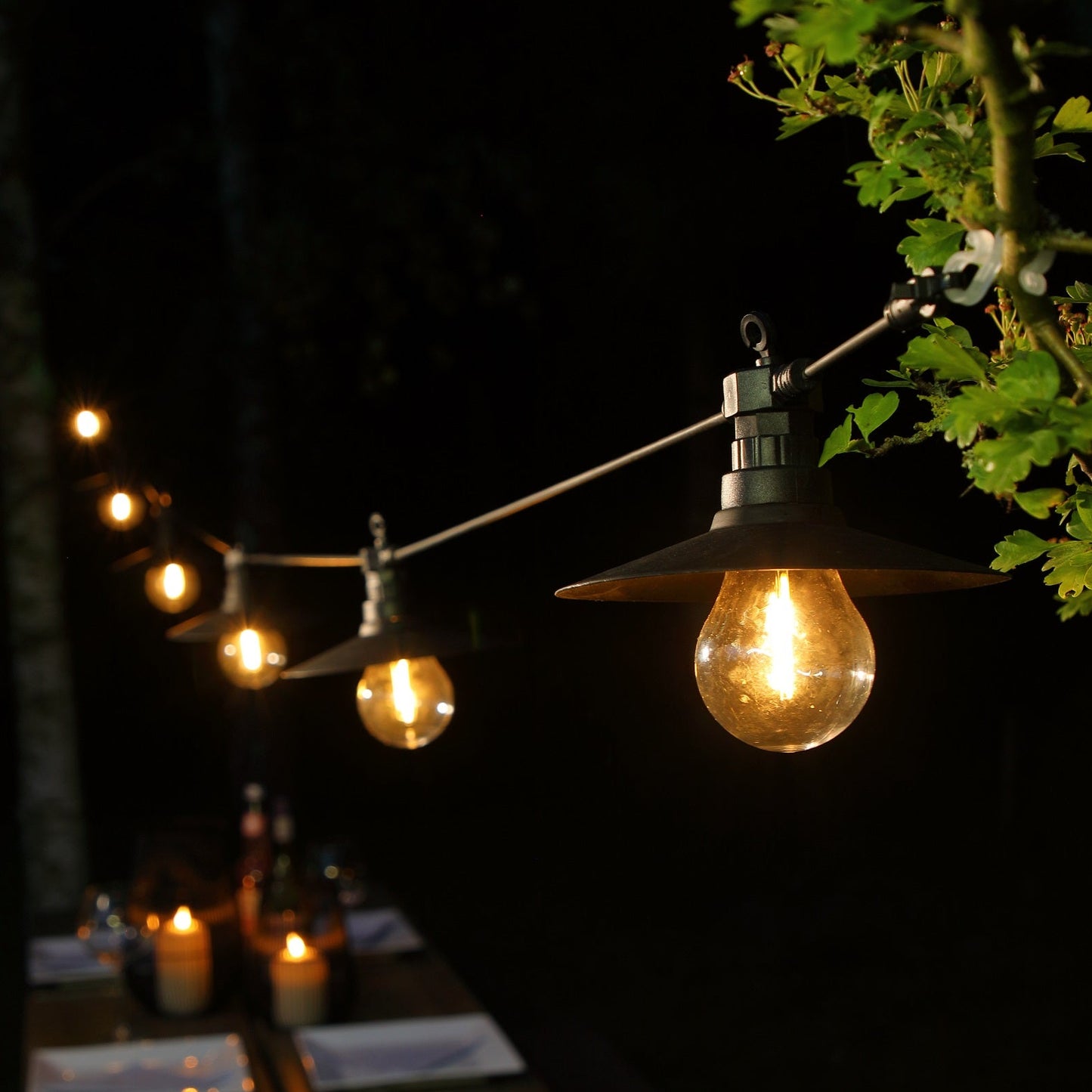 String of outdoor lights with glowing bulbs hanging above a table at night.