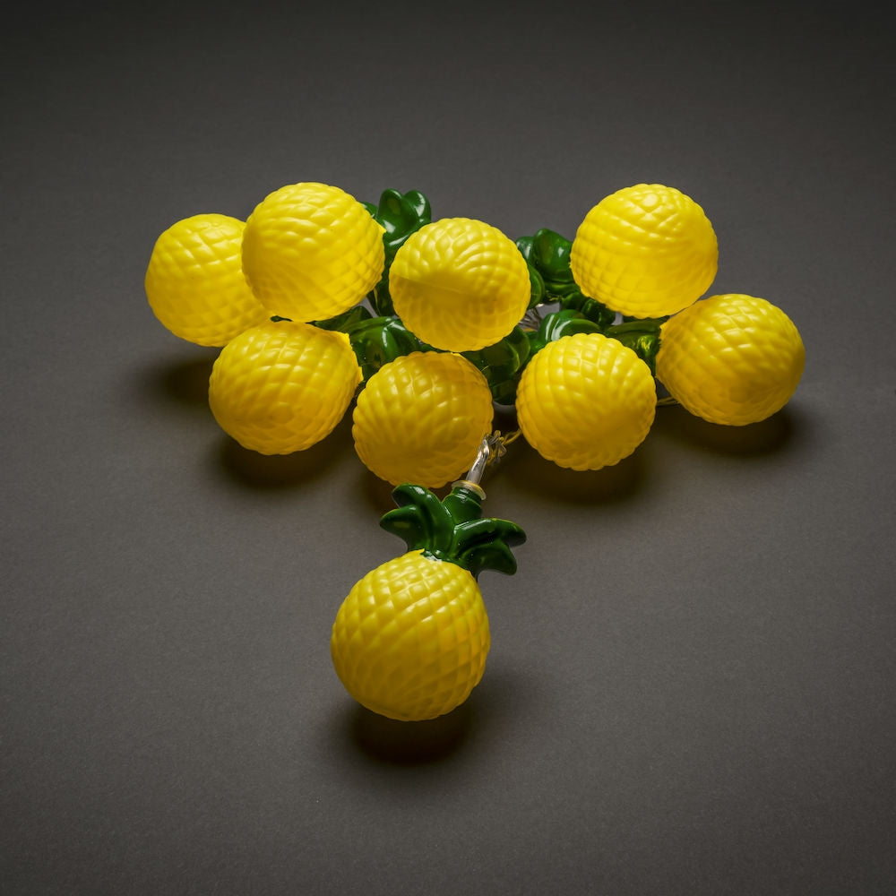 yellow pineapple lights with a green top lay out in a cluster on a plain grey background