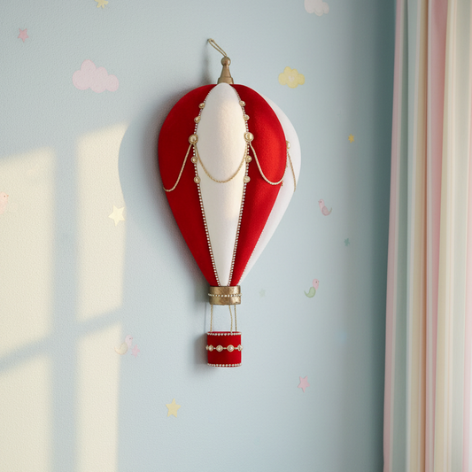 A decorative hot air balloon wall hanging plaque in red, white, and gold, mounted on a light blue wall with subtle pastel cloud and star decals.