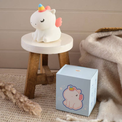 Unicorn-shaped night light on a small round table next to its packaging box.