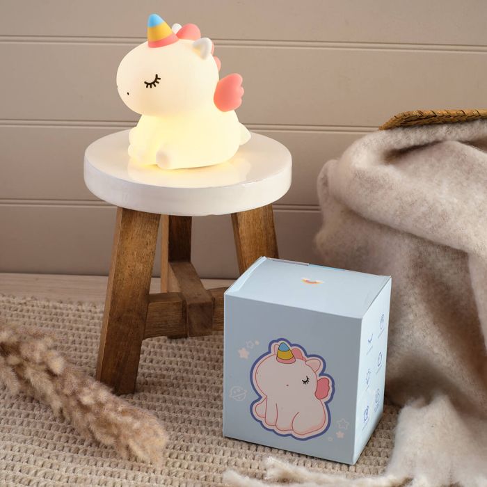 Unicorn-shaped night light on a small round table next to its packaging box.