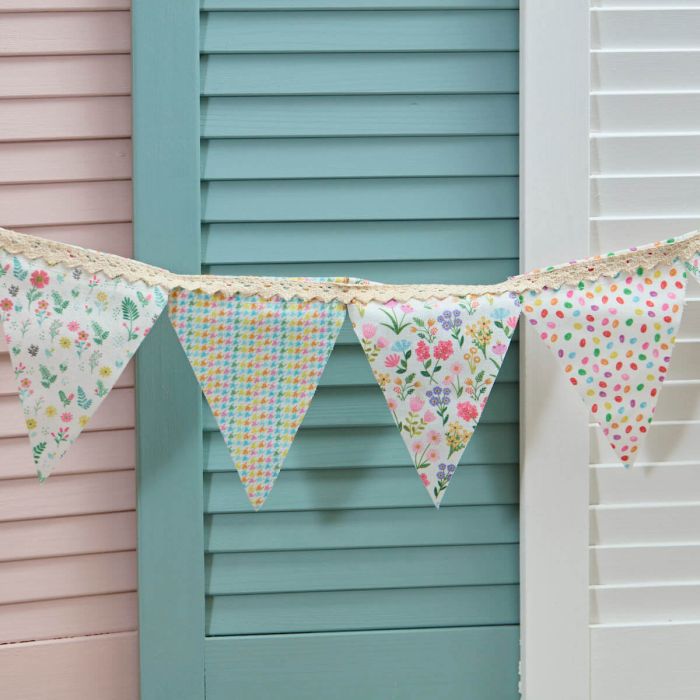 Colorful fabric bunting hanging against a pastel-colored wooden wall.