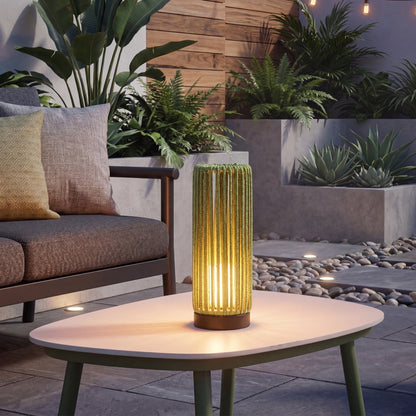Outdoor setting with a table, lamp, and seating area surrounded by plants.