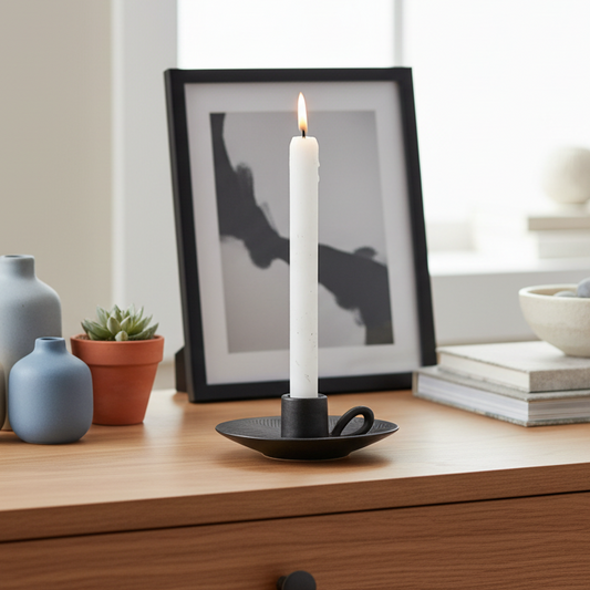 White candle in a black holder on a wooden surface with decor items.