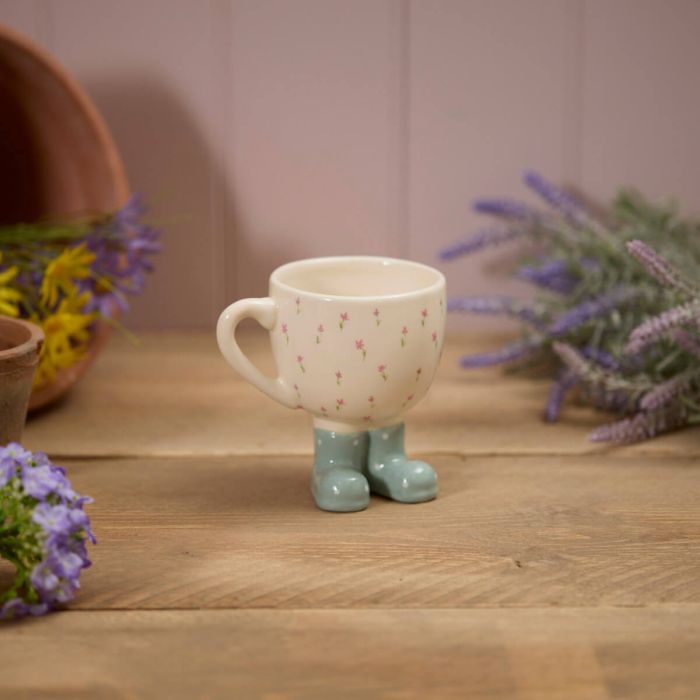 Ceramic cup with green boots on a wooden surface with flowers in the background