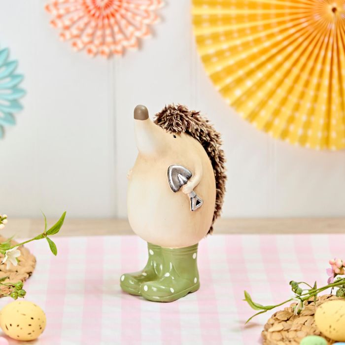Decorative hedgehog figurine wearing a green rain wellie boots with polka dots on a pink surface.