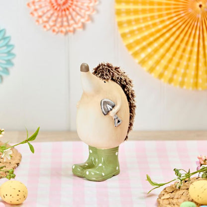 Decorative hedgehog figurine wearing a green rain wellie boots with polka dots on a pink surface.