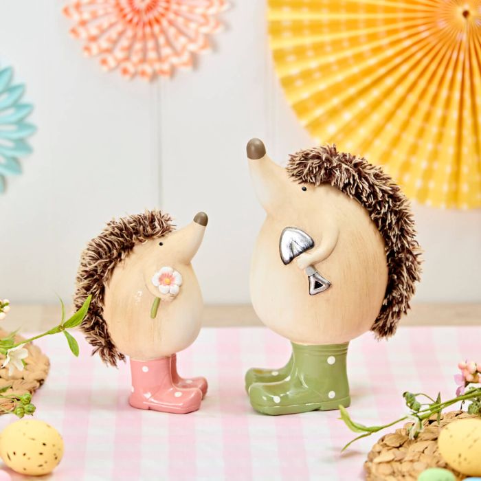 Two decorative hedgehogs with polka dot boots on a pink surface with colorful hanging decorations in the background.