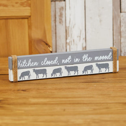 Decorative sign with cow illustrations and text on a wooden surface