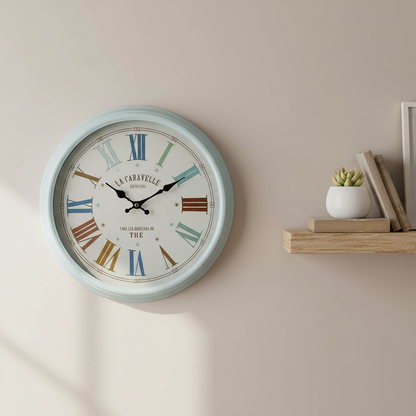 Decorative wall clock with colorful Roman numerals on a beige wall, next to a wooden shelf with books and a plant.