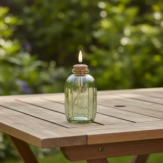 Glass bottle with cork lid containing a lit candle on a white background